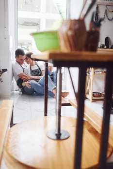 Taking a break and sitting on the floor. With her boyfriend or husband. Young female ceramist indoors with handmade clay product. Conception of pottery.