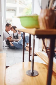 Taking a break and sitting on the floor. With her boyfriend or husband. Young female ceramist indoors with handmade clay product. Conception of pottery.