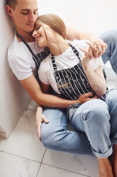 Cute young couple in jeans sitting down on the floor and embracing each other.