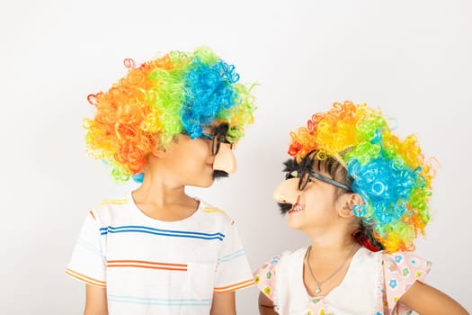 April Fool's Day. Two brothers funny kid boy and little girl clown wears curly wig colorful big nos and glasses and has mustache isolated on white background, Happy children festive decor