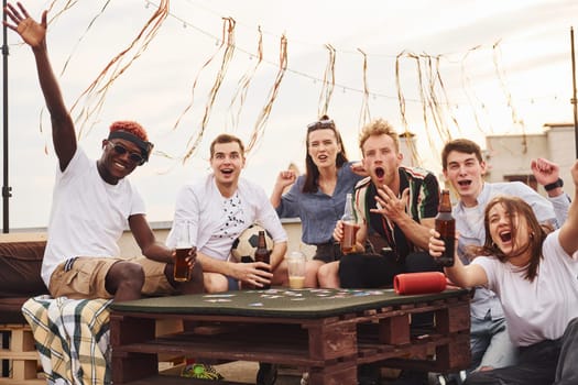 Playing card game. Group of young people in casual clothes have a party at rooftop together at daytime.