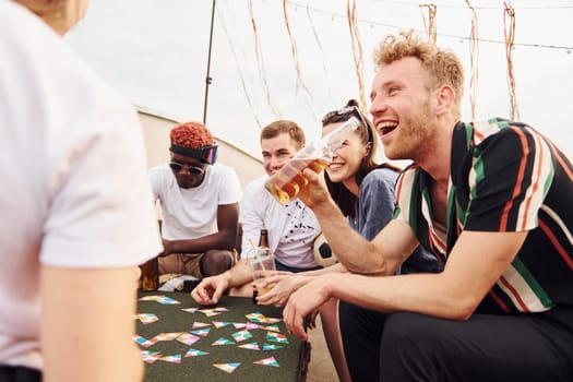 Playing card game. Group of young people in casual clothes have a party at rooftop together at daytime.