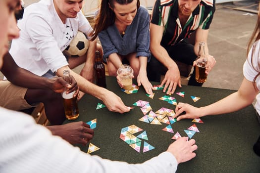 Playing card game. Group of young people in casual clothes have a party at rooftop together at daytime.