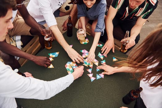 Playing card game. Group of young people in casual clothes have a party at rooftop together at daytime.