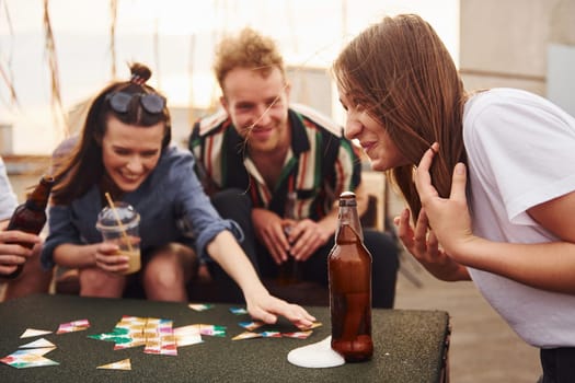 Playing card game. Group of young people in casual clothes have a party at rooftop together at daytime.