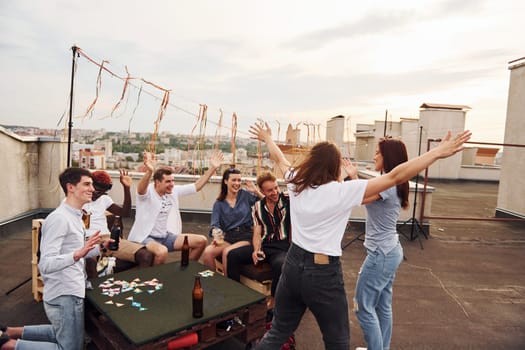 Group of young people in casual clothes have a party at rooftop together at daytime.