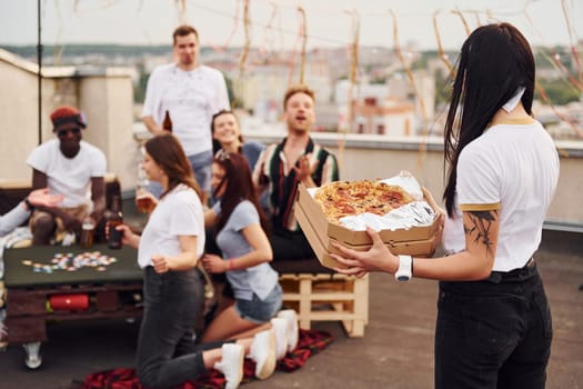 With delicious pizza. Group of young people in casual clothes have a party at rooftop together at daytime.