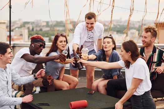 With delicious pizza. Group of young people in casual clothes have a party at rooftop together at daytime.