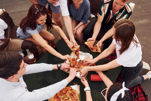 With delicious pizza. Group of young people in casual clothes have a party at rooftop together at daytime.