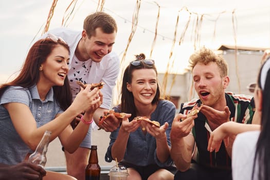 With delicious pizza. Group of young people in casual clothes have a party at rooftop together at daytime.