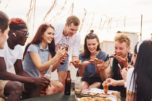 With delicious pizza. Group of young people in casual clothes have a party at rooftop together at daytime.