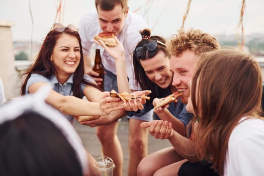 With delicious pizza. Group of young people in casual clothes have a party at rooftop together at daytime.