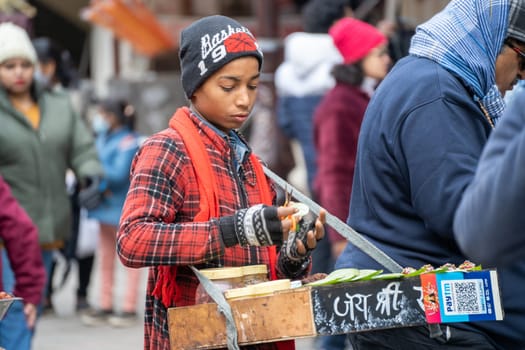 Manali, HImachal Pradesh, India - circa 2023 : Young boy sells souvenir items in a tray hanging around his neck to the tourists that crowd mall road shimla