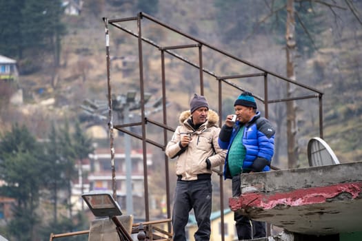 Manali, HImachal Pradesh, India - circa 2023 : Owners constuction workers sip tea on roof a new shop in manali with mountains in background