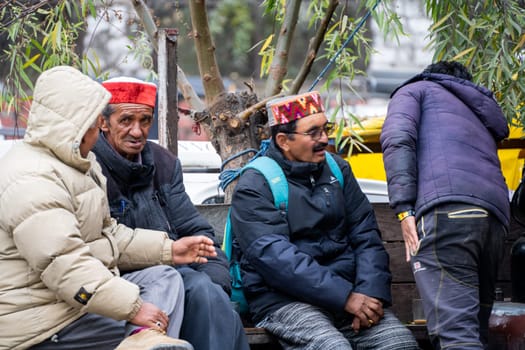 Manali, HImachal Pradesh, India - circa 2023 : Men in traditional himachal pradesh caps and jackets discuss something on the benches in mall road manali