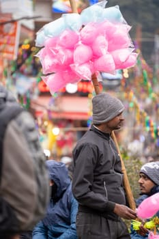 Manali, India - circa 2023: Man selling cotton candy being sold in small poly bags mounted on a stick making a cloud of candy