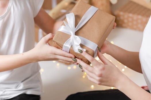 Cropped photo of Young man giving a gift box to his surprised happy woman. party moment. Hands of young boyfriend surprise in box with white ribbon to his girlfriend