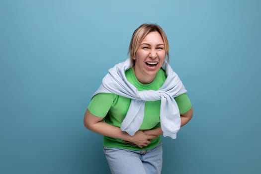 blond cheerful bright girl in a casual outfit laughing widely until her stomach hurts on a blue background with copy space.