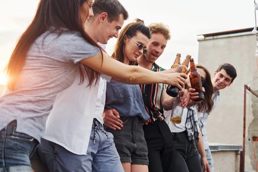 Leaning on the edge of the rooftop with decorates. Group of young people in casual clothes have a party together at daytime.