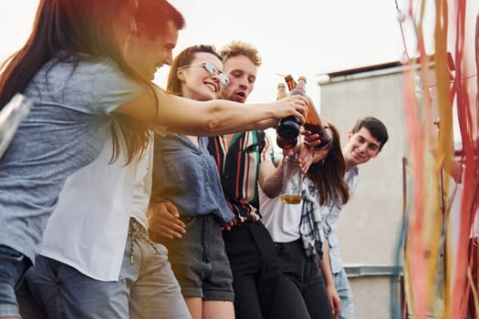Leaning on the edge of the rooftop with decorates. Group of young people in casual clothes have a party together at daytime.