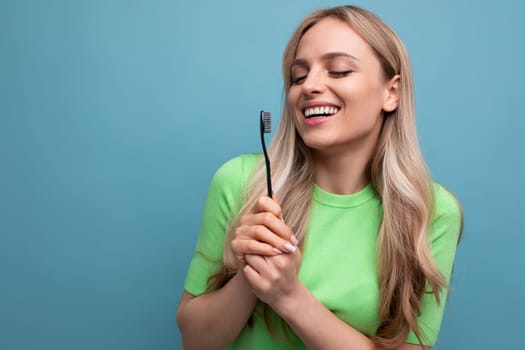 healthy young blond woman with even teeth holding a toothbrush on a blue background.