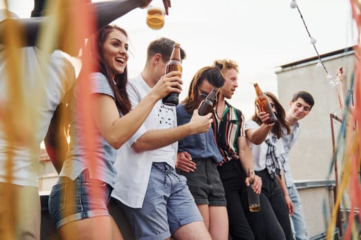 Leaning on the edge of the rooftop with decorates. Group of young people in casual clothes have a party together at daytime.