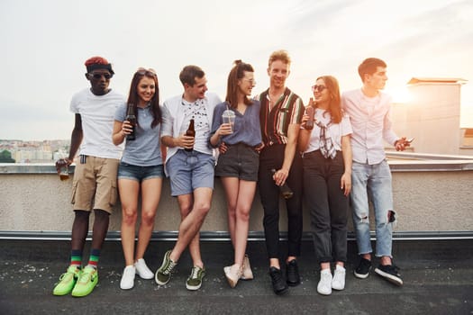 Standing with alcohol at the edge of rooftop. Group of young people in casual clothes have a party together at daytime.