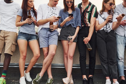 Standing with alcohol at the edge of rooftop. Group of young people in casual clothes have a party together at daytime.