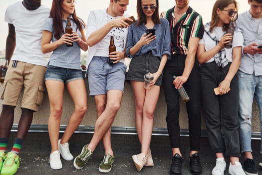 Standing with alcohol at the edge of rooftop. Group of young people in casual clothes have a party together at daytime.