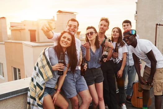 Taking selfie. Beautiful sunshine. Group of young people in casual clothes have a party at rooftop together at daytime.