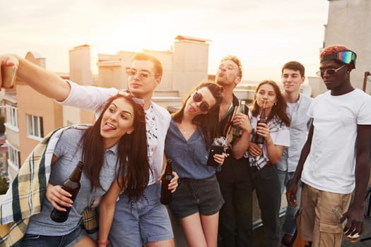 Taking selfie. Beautiful sunshine. Group of young people in casual clothes have a party at rooftop together at daytime.