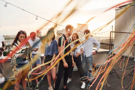 Group of young people in casual clothes have a party at rooftop together at daytime.