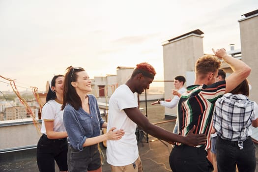 Recreation time. Group of young people in casual clothes have a party at rooftop together at daytime.