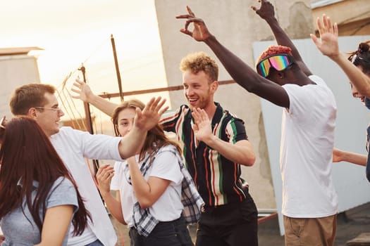 Recreation time. Group of young people in casual clothes have a party at rooftop together at daytime.