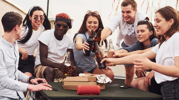 Delicious pizza. Group of young people in casual clothes have a party at rooftop together at daytime.