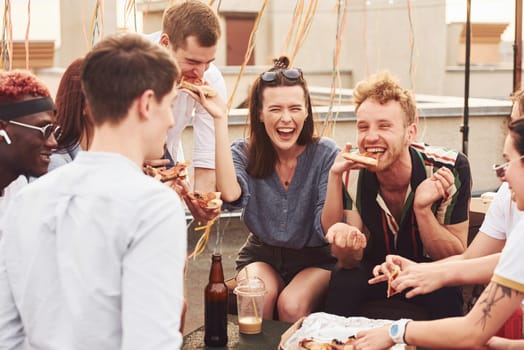 Delicious pizza. Group of young people in casual clothes have a party at rooftop together at daytime.