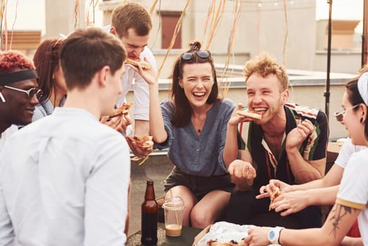 Delicious pizza. Group of young people in casual clothes have a party at rooftop together at daytime.