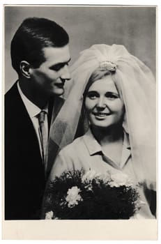 BRATISLAVA, THE CZECHOSLOVAK SOCIALIST REPUBLIC - DECEMBER 11, 1965: Retro photo shows bride wears a white veil and groom wears a dark suit. Black and white vintage photography of wedding couple.