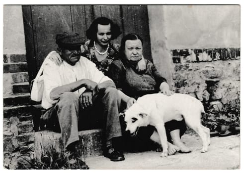 THE CZECHOSLOVAK SOCIALIST REPUBLIC - CIRCA 1960s: Retro photo shows rural people sit on a doorstep with dog. Black and white vintage photography