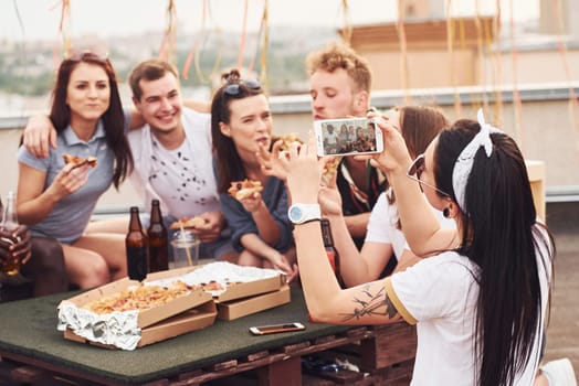 Making photo. Delicious pizza. Group of young people in casual clothes have a party at rooftop together at daytime.