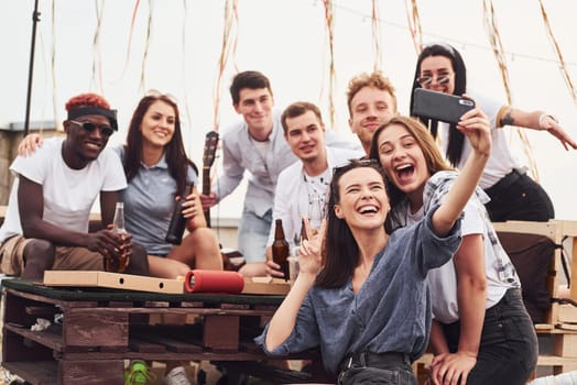 Making photo. Delicious pizza. Group of young people in casual clothes have a party at rooftop together at daytime.