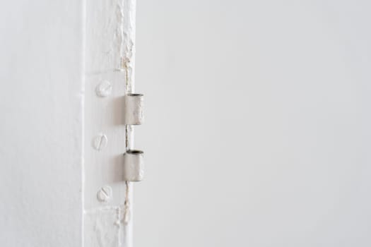 Detailed view of an antique hinge without a door, showing its rusty steel surface and hidden screws painted over on a white wall.