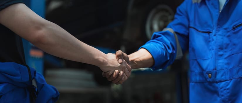 Young man client shaking hands with auto mechanic in red uniform having a deal at the car service.