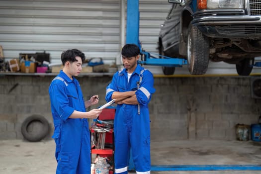 Mechanic man shows report to the asian coworker at garage, A man mechanic and his son discussing repairs done vehicle. Changing automobile business..