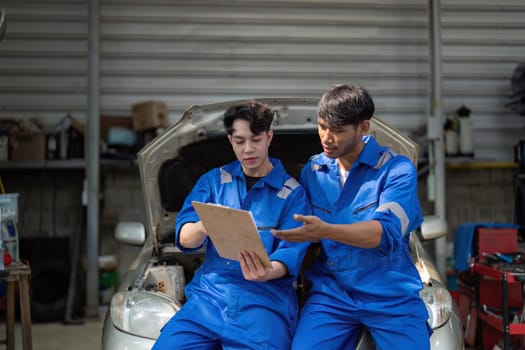 Mechanic man shows report to the asian coworker at garage, A man mechanic and his son discussing repairs done vehicle. Changing automobile business..