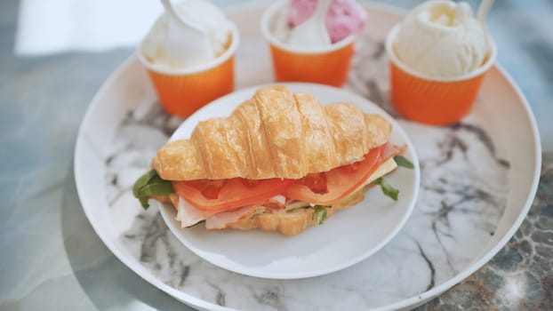Ice cream and croissant with meat on the plate at the cafe