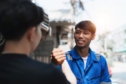 Young man client shaking hands with auto mechanic in red uniform having a deal at the car service.