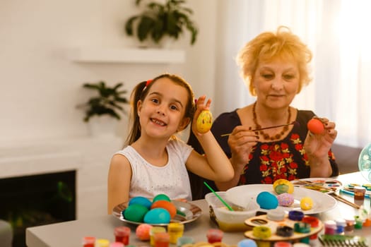 Little girl and her grandmother painting Easter eggs at home