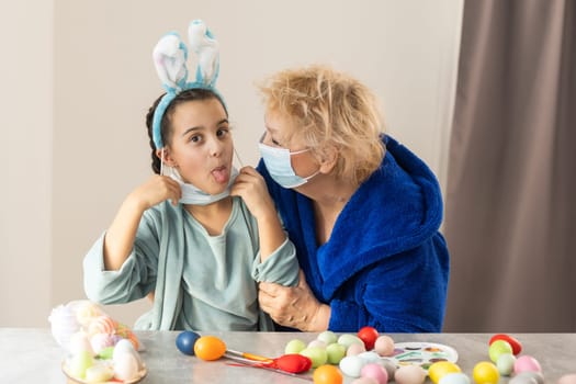 grandmother and children are painting eggs. Happy family are preparing for Easter. Cute little girls wearing bunny ears