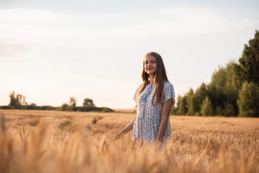 Beautiful teenage girl walking in field of ripe wheat